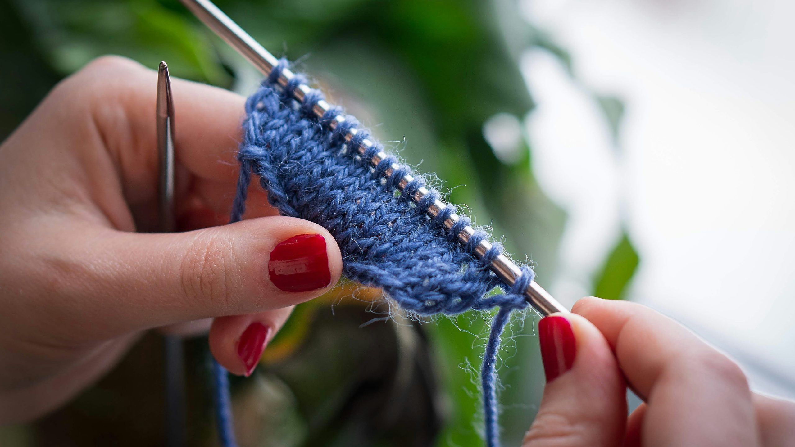 Close-up of hands knitting blue yarn with metal knitting needles in a row.