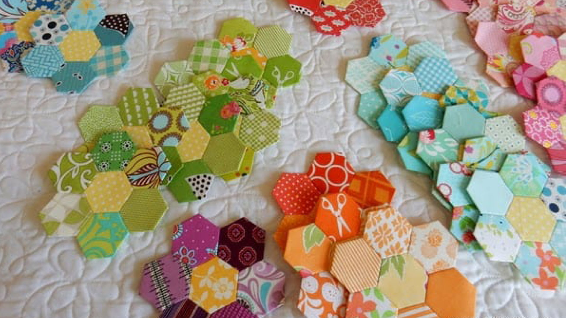 Colorful hexagon fabric scraps arranged in a honeycomb quilt on a white background.