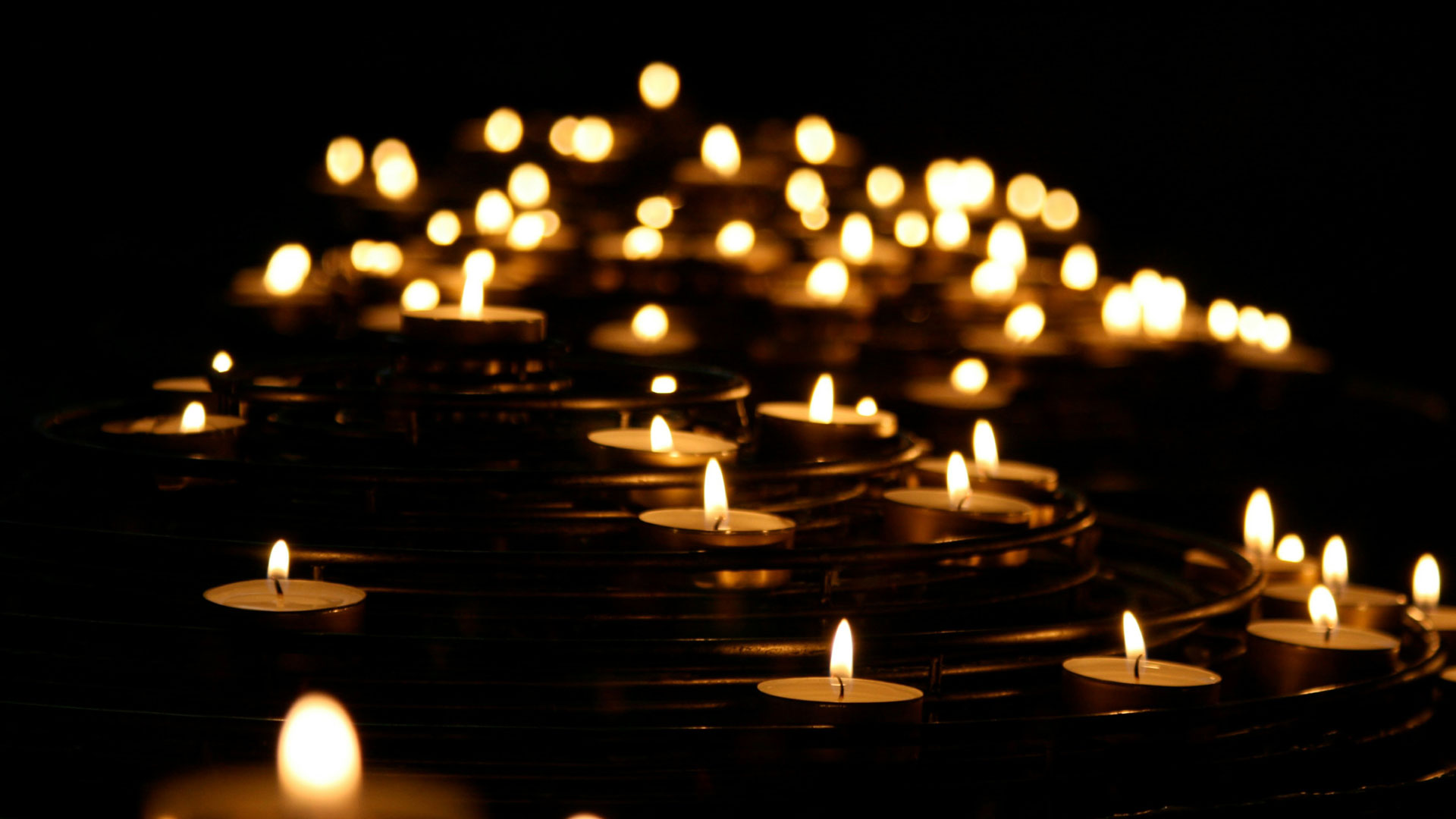 Row of lit tealight candles floating on dark water, creating warm bokeh lights in the background.