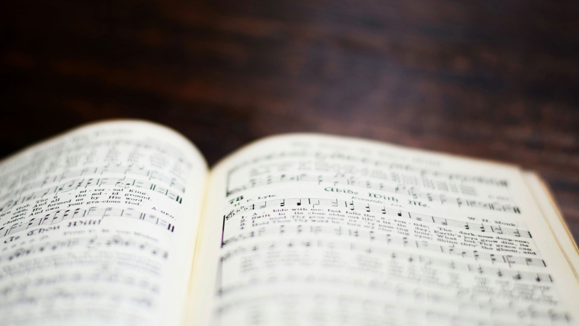 Open book showing sheet music and lyrics, close-up on a dark wooden surface.