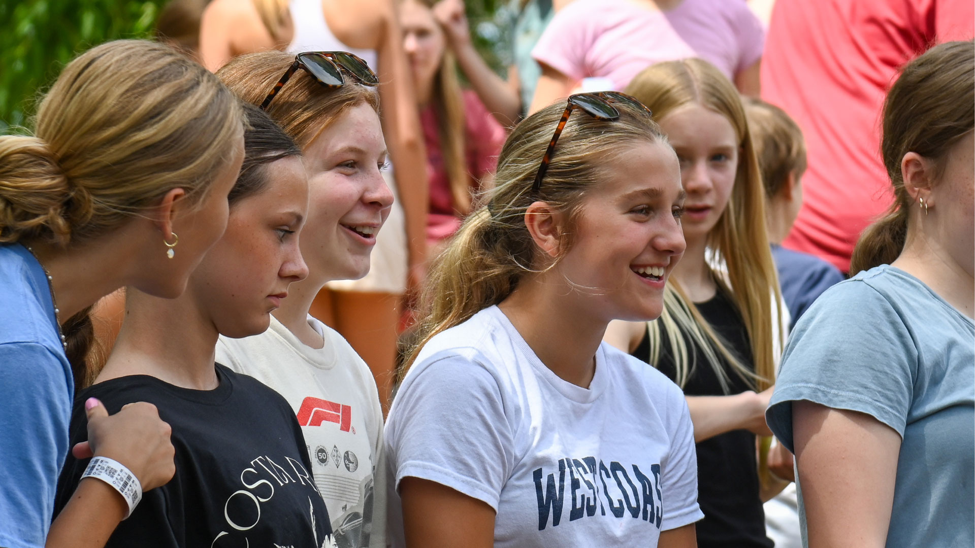 Group of smiling teenagers standing together at an outdoor event, wearing casual T-shirts.