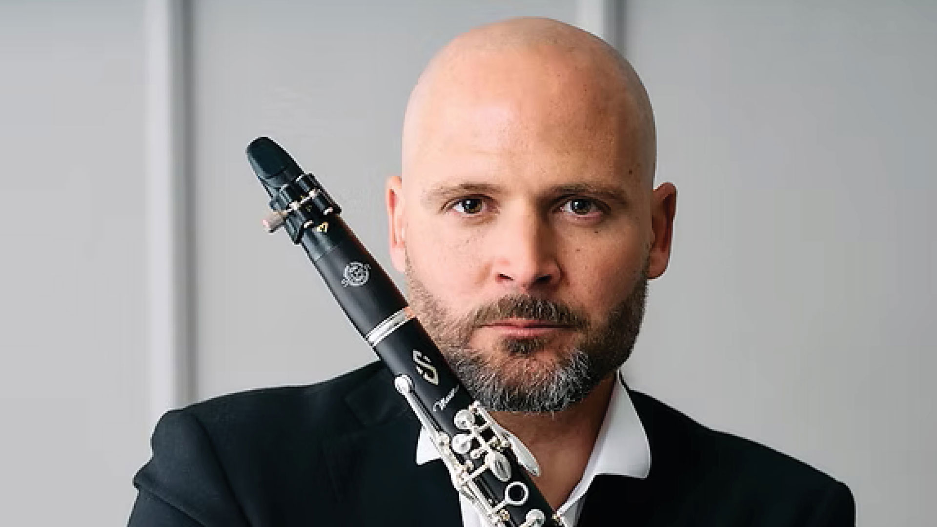 Man in a suit posing with a clarinet resting on his shoulder, looking at the camera.