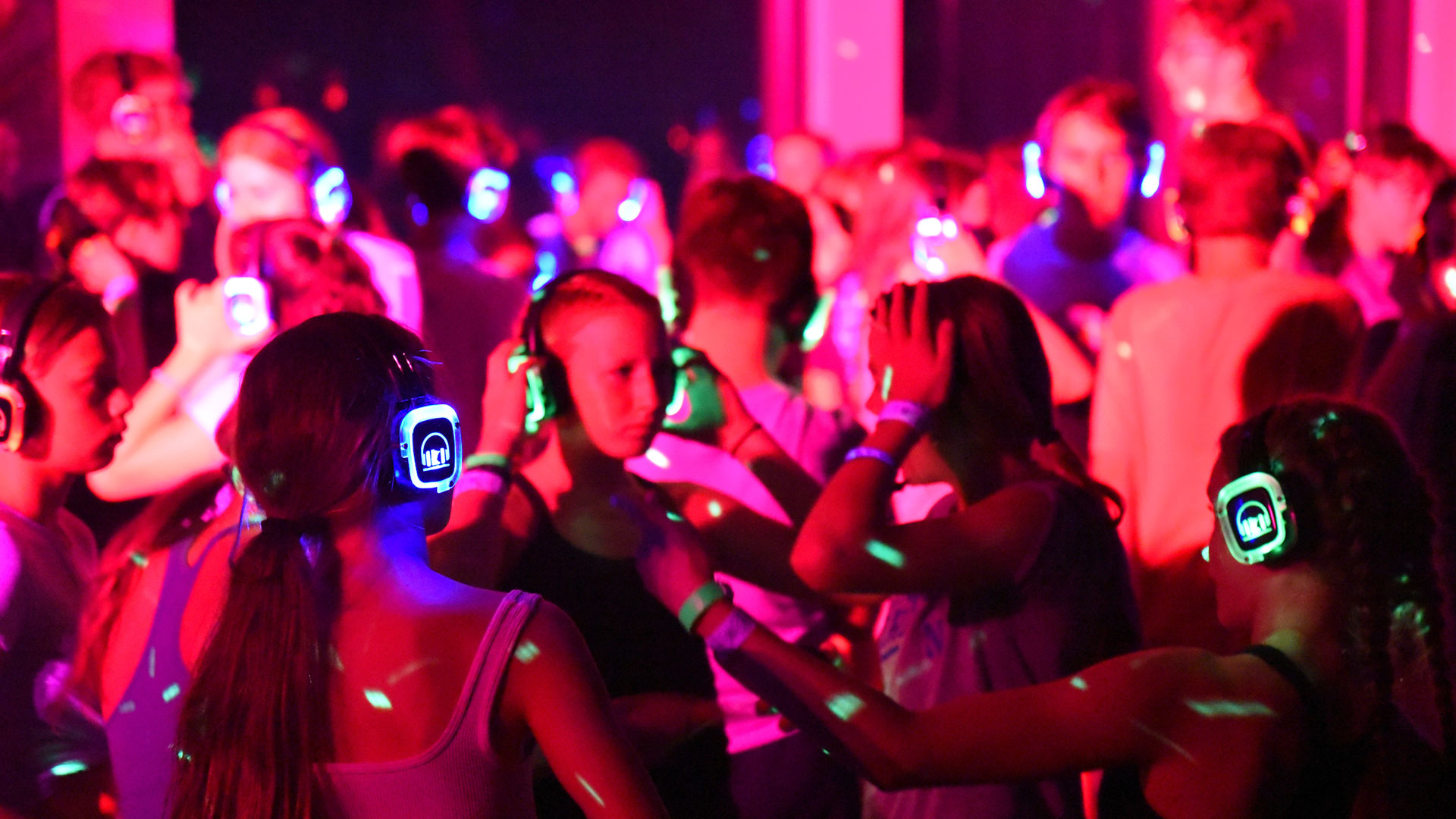 Crowd dancing at a neon-lit silent disco wearing glowing headphones