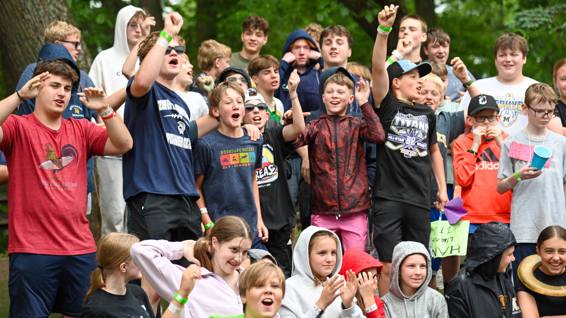 Large group of kids cheering and posing together at an outdoor camp event.